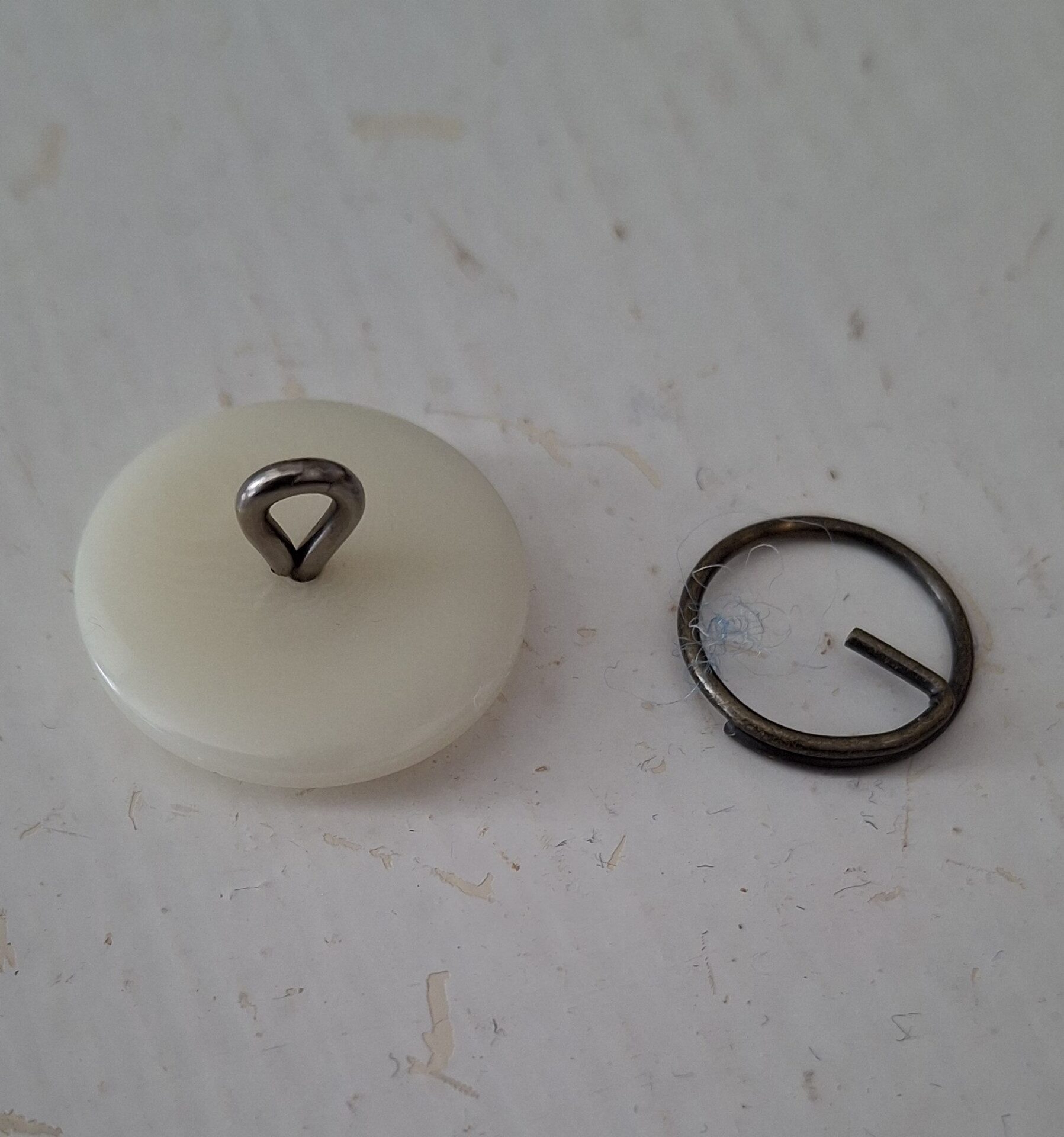 A single vintage brass button with a hand-worked pattern, resting on pale paper.