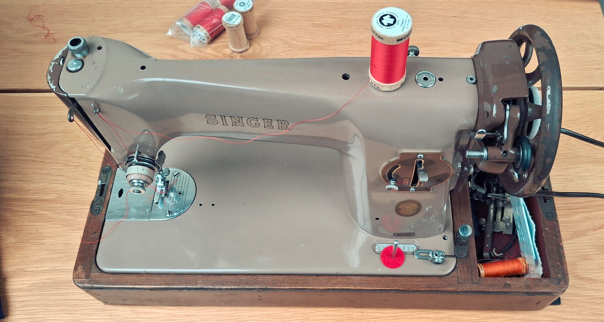 A vintage Singer sewing machine with a red spool of thread, resting on a wooden tabletop.